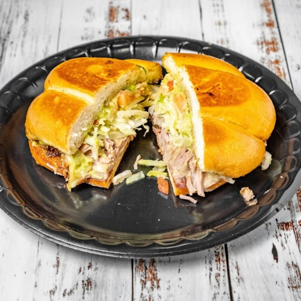 A Bandeño Mexican Food torta, sliced in half, revealing savory meat, lettuce, and tomato.