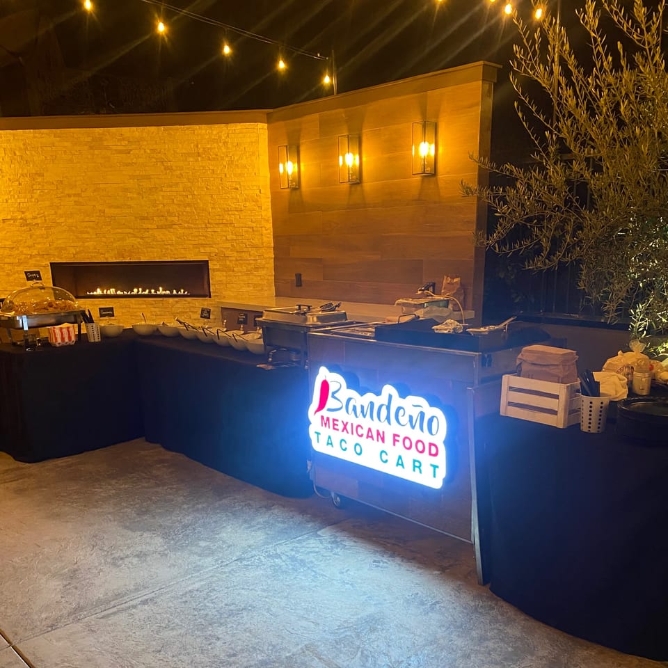 Bandeño Mexican Food taco cart with a glowing sign, buffet, and fireplace at night.
