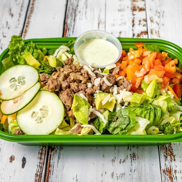 Bandeño Mexican Food's vibrant salad with beef, avocado, cucumber, tomato, and dressing in a green container.