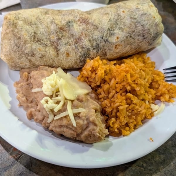 A Bandeño Mexican Food burrito with a side of refried beans topped with cheese and Mexican rice.