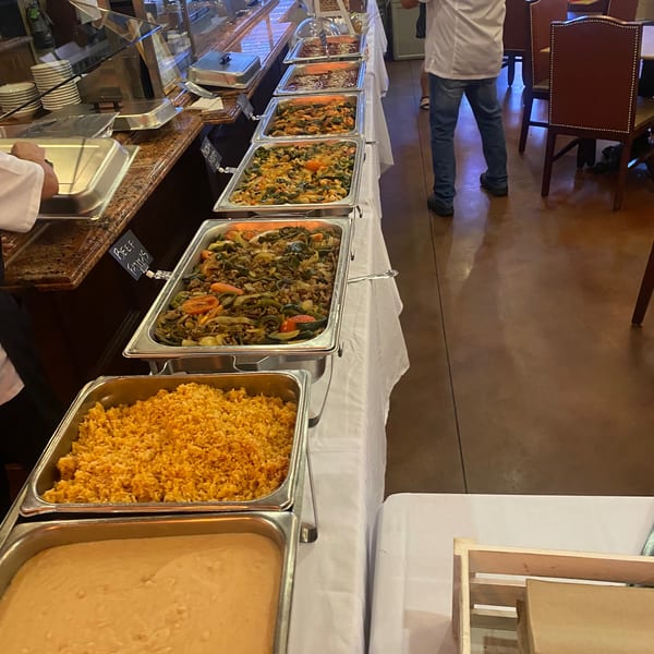 A long buffet table filled with various Mexican dishes in metal serving trays, including rice and fajitas.
