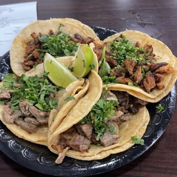 Four Bandeño Mexican Food tacos with meat, cilantro, and lime wedges on a black plate.